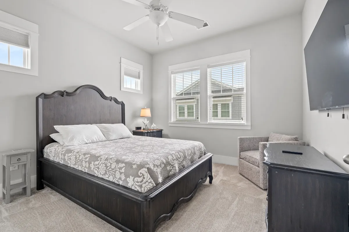 A serene bedroom with a plush bed, nightstand, armchair, and large windows. Sunlight fills the room, and the setup invites both relaxation and comfort—ideal for a midday nap, reading, or unwinding after a long day.
