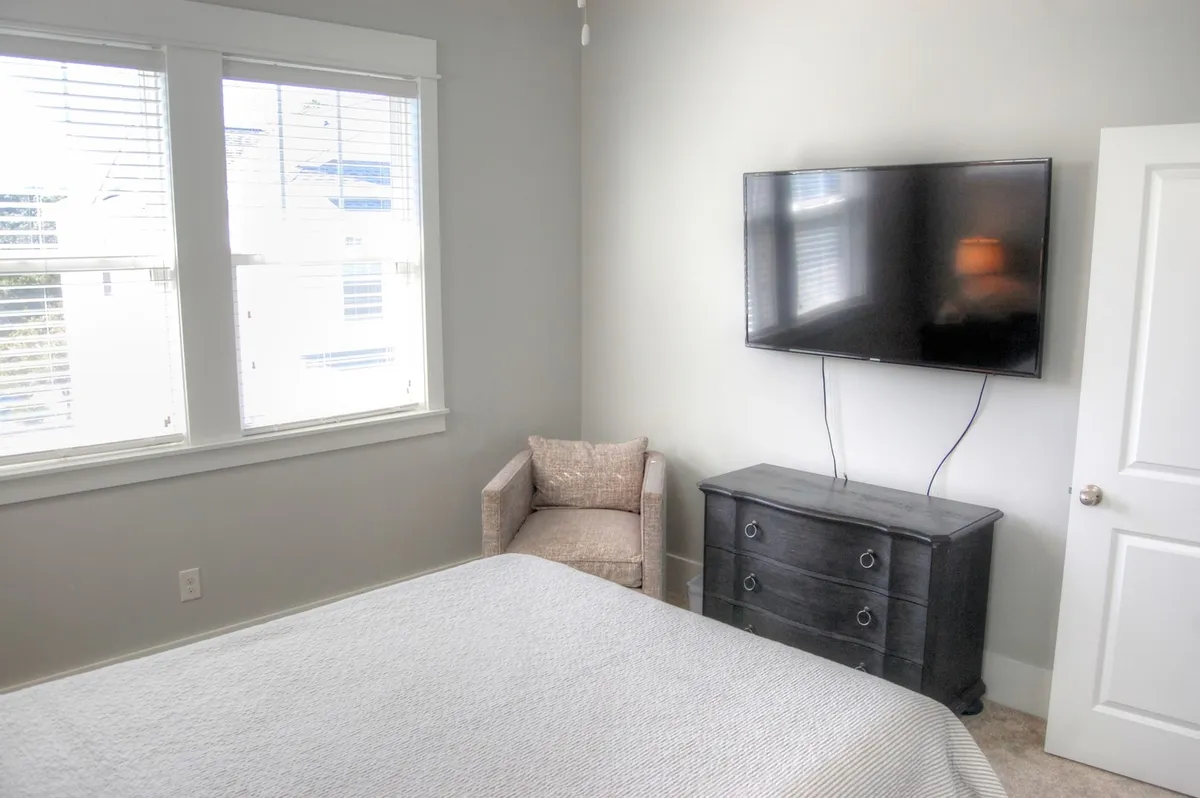 A cozy bedroom featuring a comfortable bed, television, armchair, and dresser. The room is bright and appealing, offering both comfort and convenient entertainment options, reflecting the owner's mention of flat-screen TVs in every bedroom.