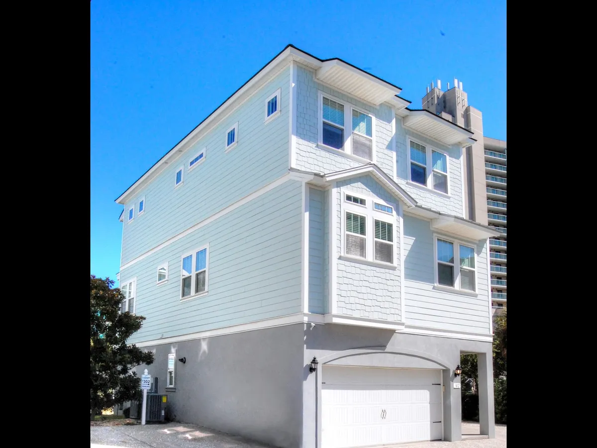 A welcoming exterior shot of a light blue house featuring multiple windows, distinct architectural details on the roof, and an inviting porch. The scene hints at communal outdoor relaxation and a home base perfectly suited for social gatherings, with the vibrant city atmosphere just beyond.