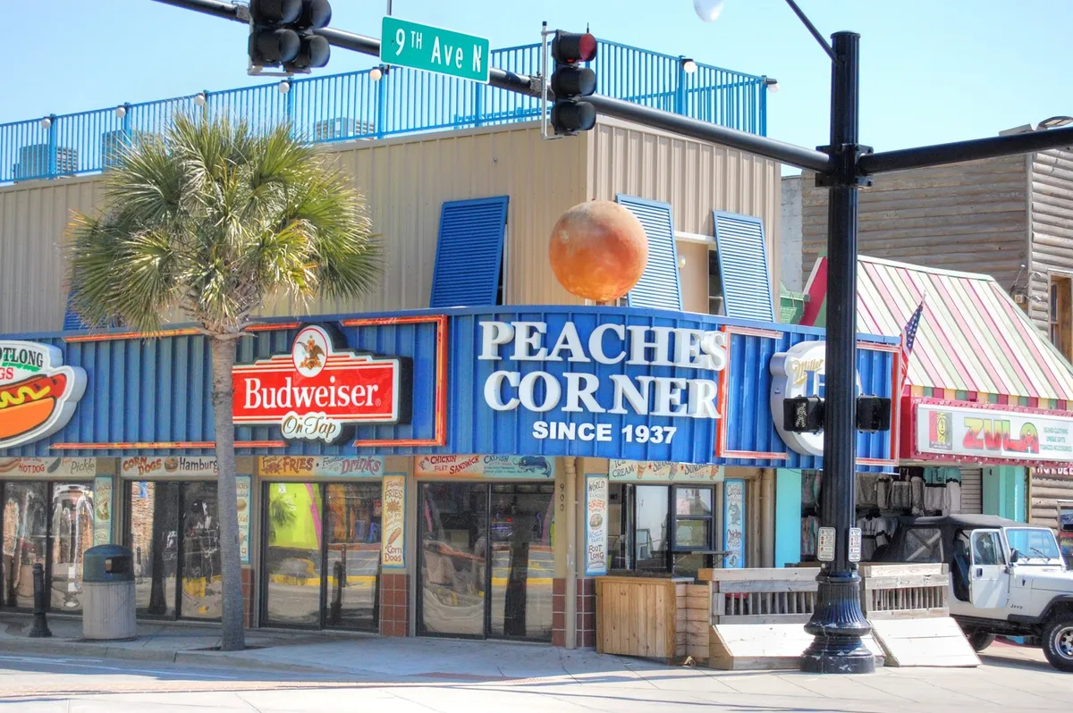 A lively street scene outside Peaches Corner, featuring bright signage, outdoor seating, and a bustling sidewalk with social interactions. The presence of palm trees and neon lights hint at the vibrant energy and ongoing nightlife of Myrtle Beach.