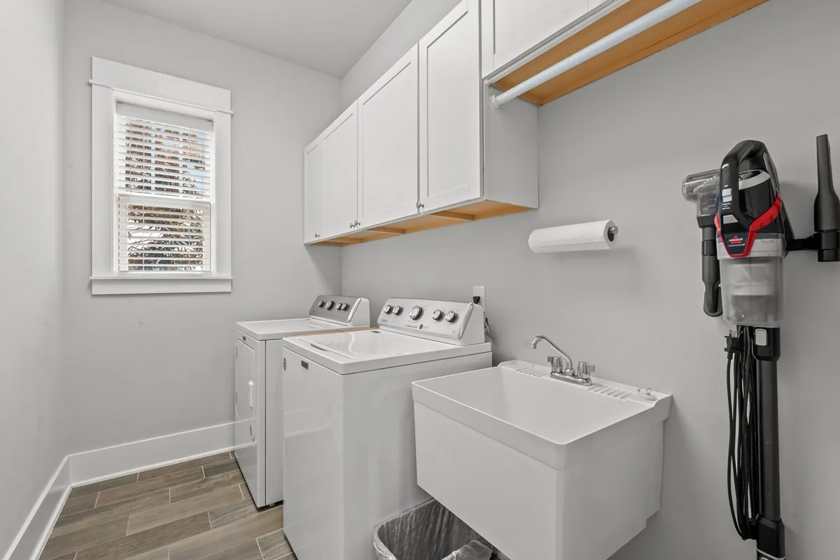 A bright and practical laundry room featuring a washer, dryer, utility sink, and ample cabinetry. The space is organized and efficient, with plenty of storage to keep laundry essentials tidy and within reach.