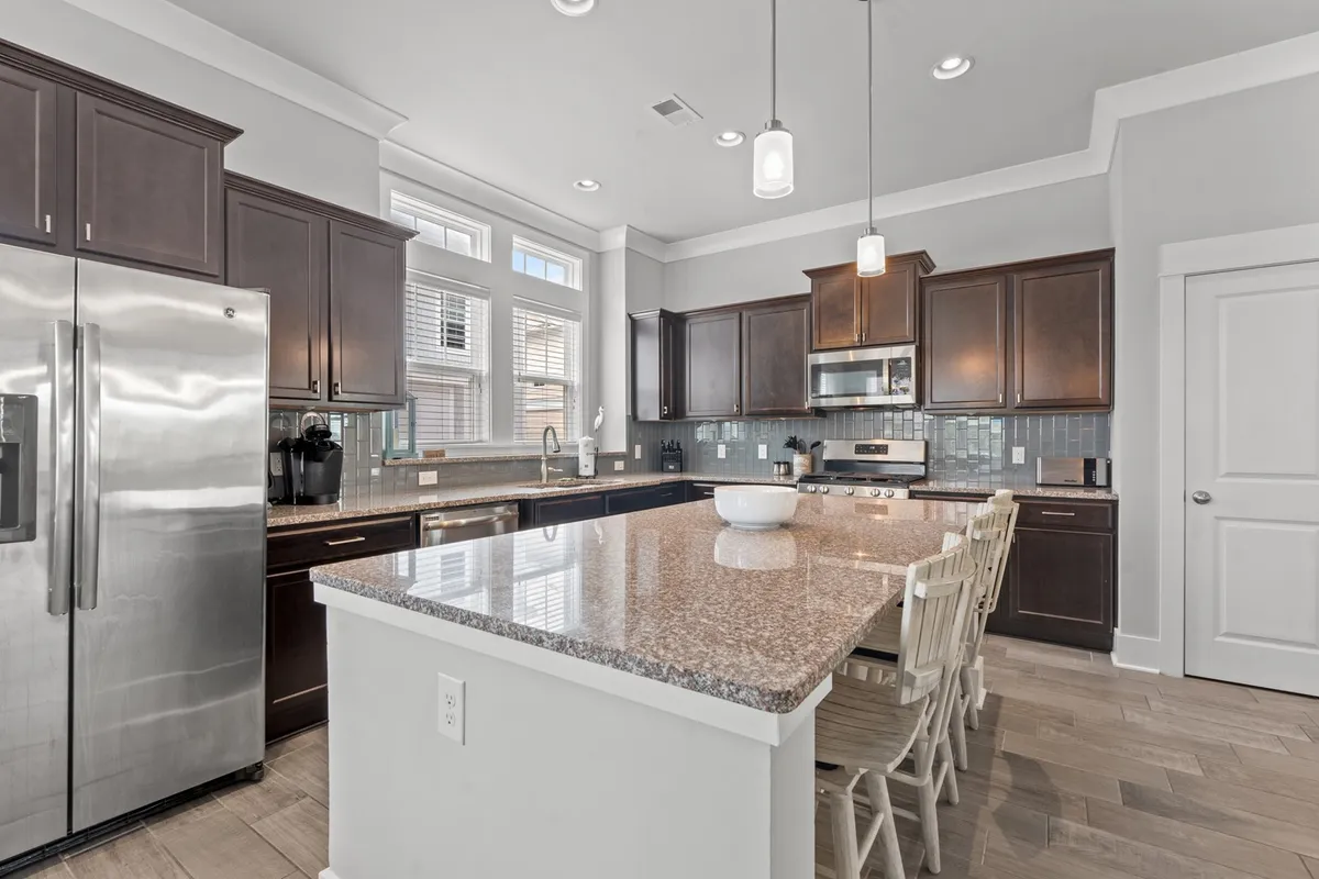 A modern kitchen with a prominent island, stainless steel appliances, granite countertops, and white cabinetry. The kitchen is designed for both functionality and style, inviting guests to cook, gather, and enjoy shared culinary adventures.