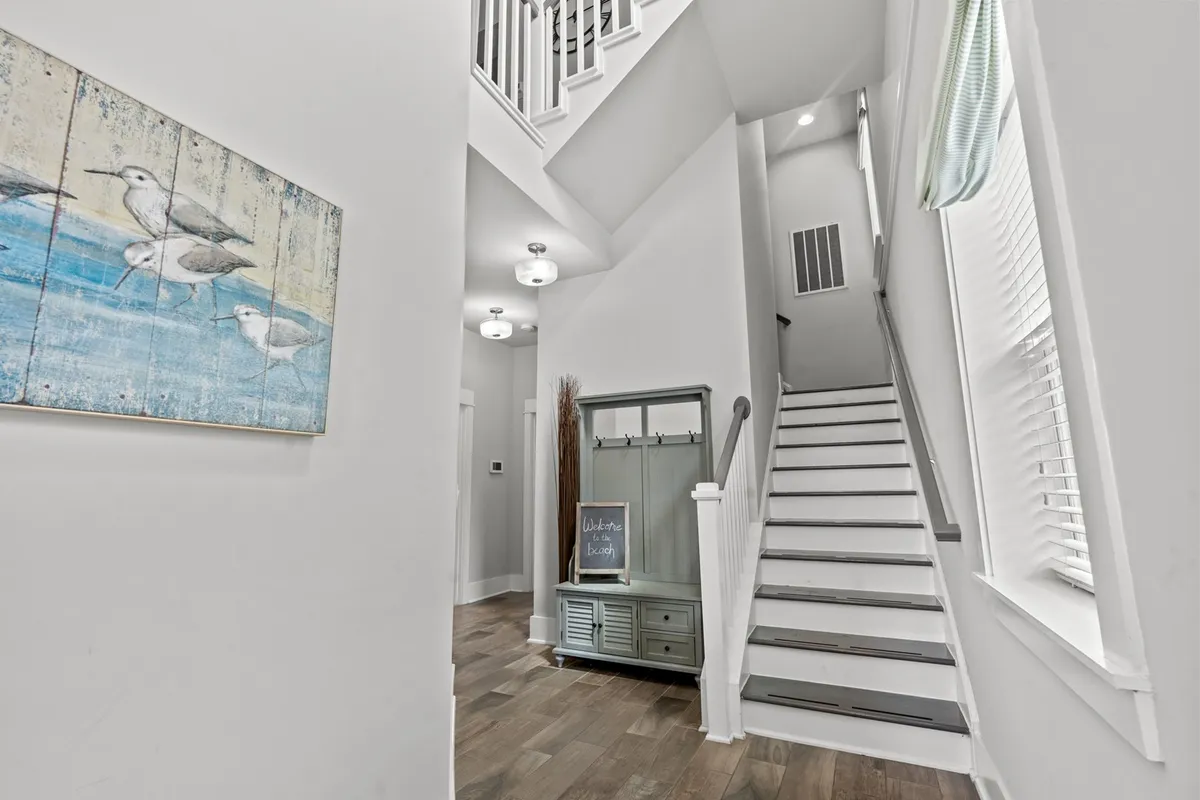 A welcoming entryway featuring a staircase, a 'welcome' sign, coastal-themed artwork, and a convenient entry console. The space feels both inviting and accessible, embodying the comfort of a private home.
